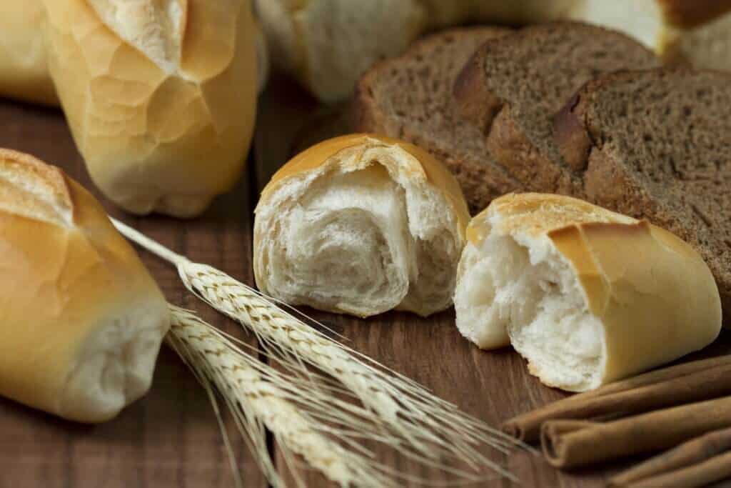 Various types of bread, wheat stalks, and cinnamon sticks are artfully arranged on a wooden surface, highlighting a rustic, natural setting.
