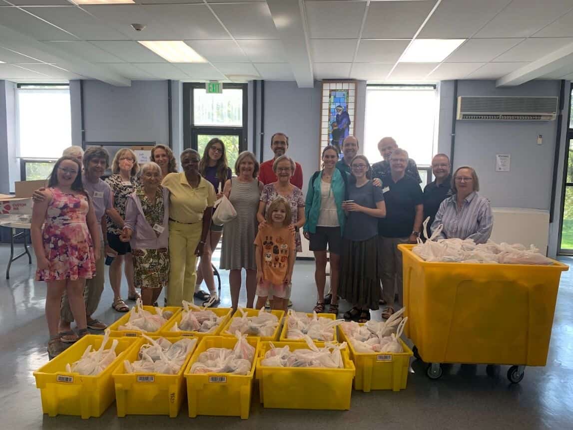 A group of people in a room pose with yellow bins filled with bags, possibly for a community service or donation event.