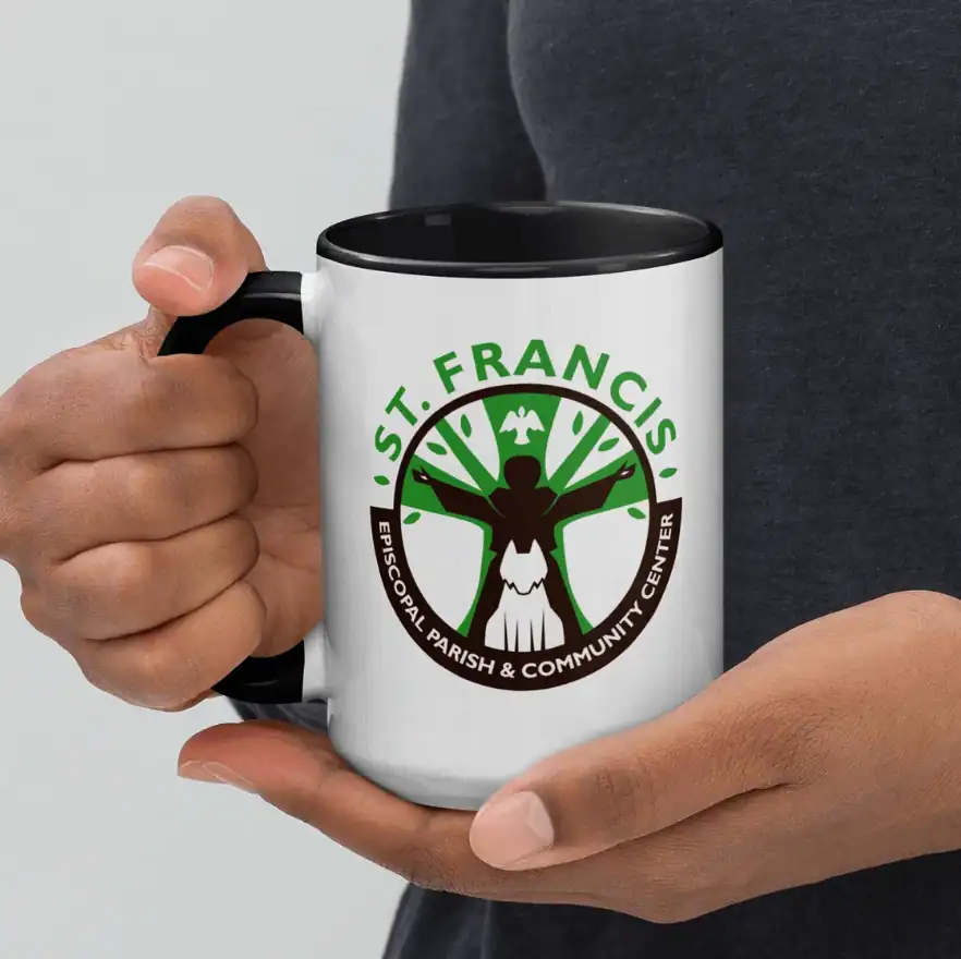 A person holds a white mug featuring the St. Francis Episcopal Parish & Community Center logo, displaying a stylized tree and dove design.